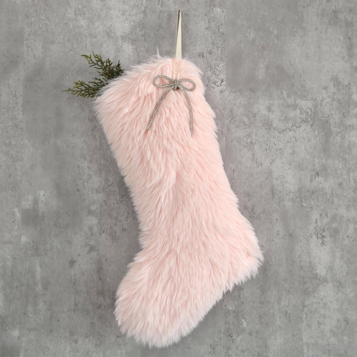 A pink furry stocking with a bow tied around it, hanging on a gray wall.