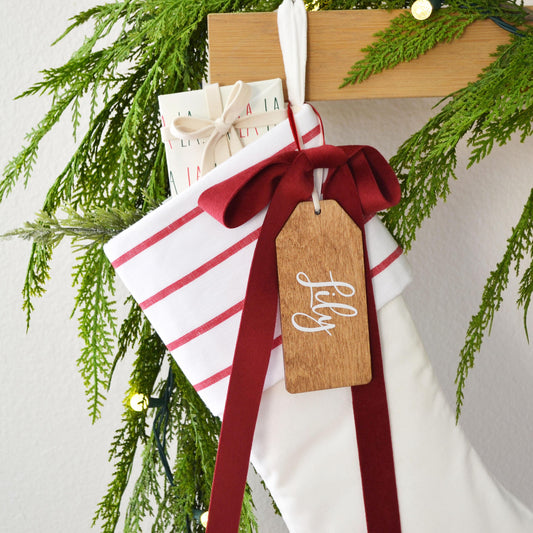 A white and red striped stocking with a red ribbon and a wooden tag with the name "Lily" written on it, hanging on a wooden hanger.