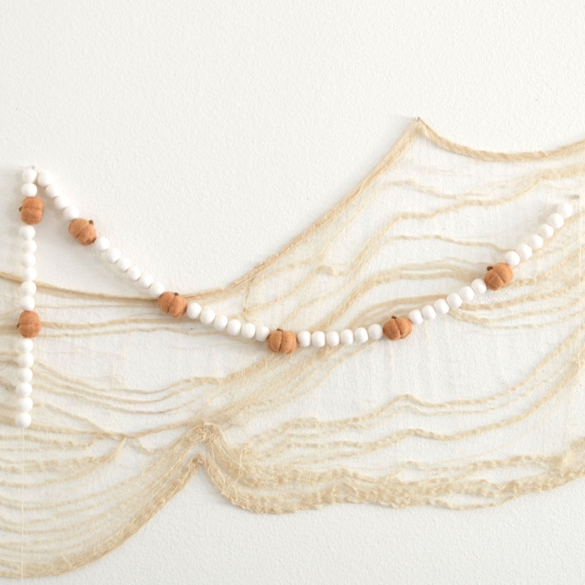 A string of white beads with small orange beads attached, hanging against a white background.