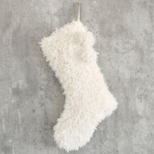 A fluffy white Christmas stocking is hanging on a gray wall.