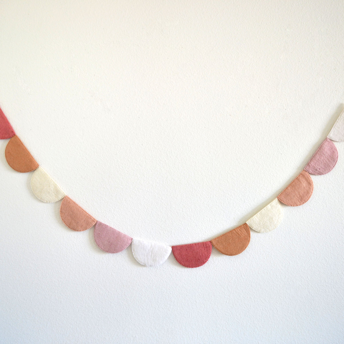 A decorative garland made of fabric circles in various pastel colors, including pink, white, and orange, hanging on a white wall.