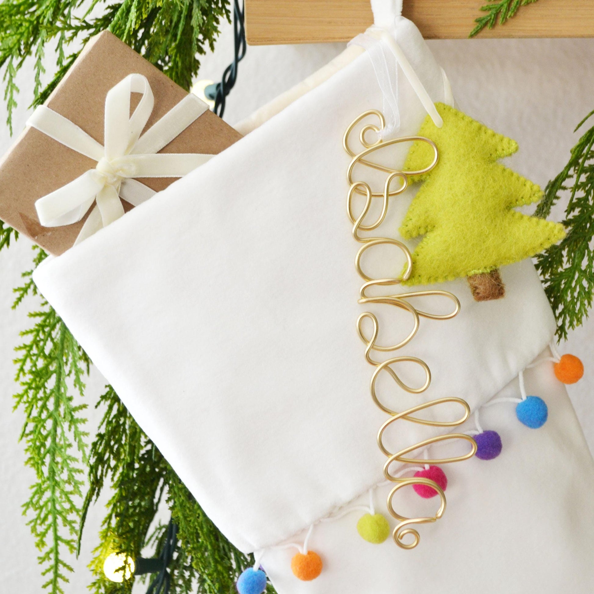 A white Christmas stocking decorated with a green felt tree ornament, a gift box, and a personalized name charm.
