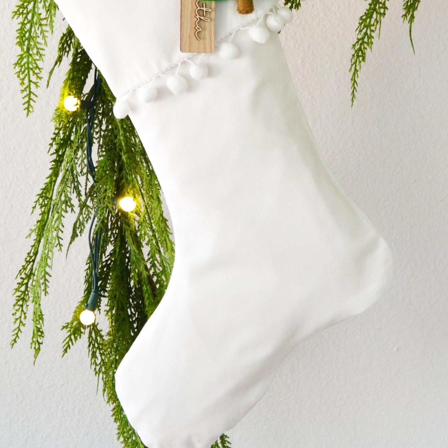 A white Christmas stocking decorated with green pine branches and twinkling lights, creating a festive and cozy atmosphere.