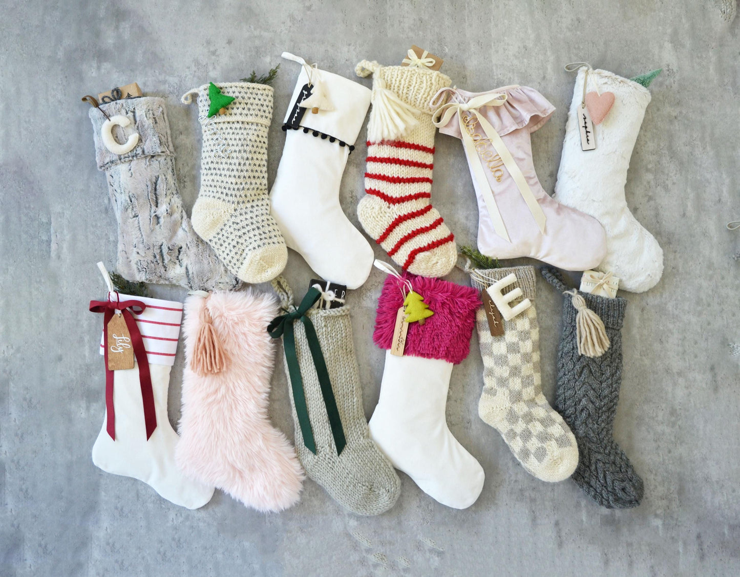 A collection of variously colored and patterned Christmas stockings, some with ribbons and others with tassels, arranged on a gray surface.