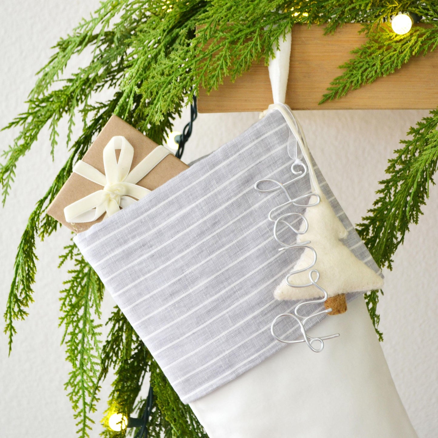 A white and gray striped stocking hanging on a wooden hanger, decorated with a ribbon and a small white ornament.